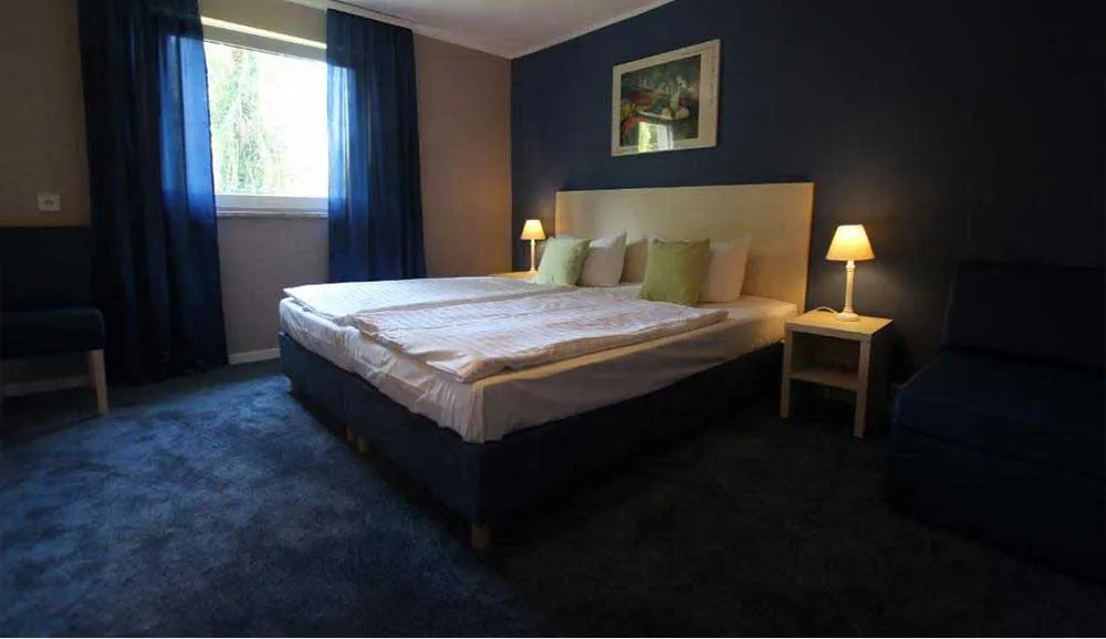 Geräumiges Doppelzimmer mit großem Doppelbett, zwei Nachttischlampen und Sessel