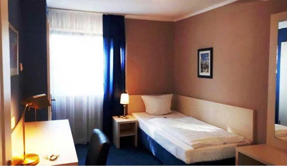 Einzelzimmer mit Einzelbett, Schreibtisch, Leselampe und blauen Vorhängen