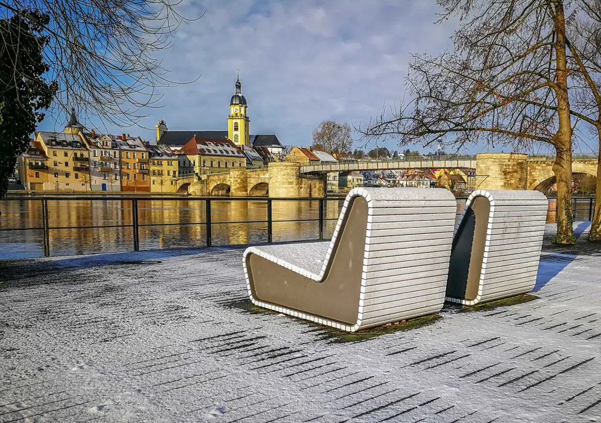 Alte Mainbrücke und Altstadt von Kitzingen im Winter, vorne zwei Sitzliegen am Mainufer